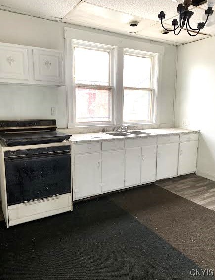 kitchen featuring white cabinets, light countertops, a chandelier, a sink, and electric range