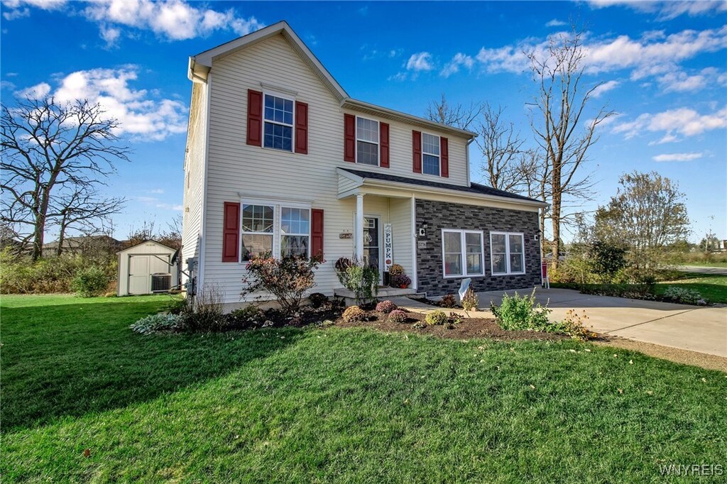 5774 Willow Creek Ln, Cambria, NY 14132 - traditional-style house with a front yard, concrete driveway, central air condition unit, a shed, and an outbuilding