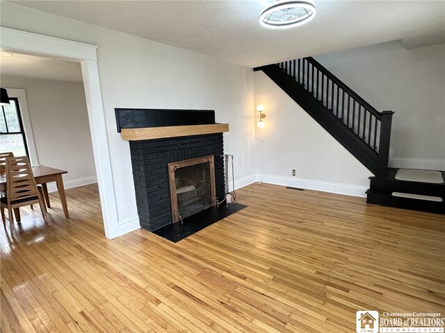 3514 Lake St, Ellicott, NY 14701 - unfurnished living room featuring a textured ceiling, a brick fireplace, baseboards, stairway, and wood-type flooring