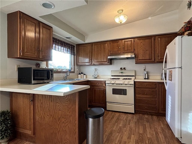 kitchen with vaulted ceiling, a peninsula, dark wood finished floors, under cabinet range hood, and white appliances