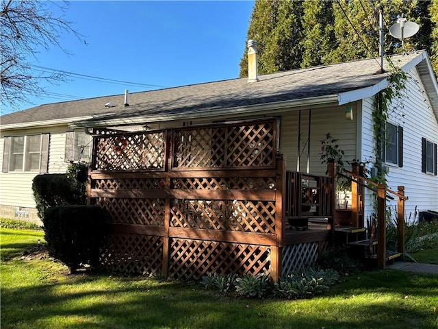 rear view of property featuring roof with shingles, a deck, and a lawn