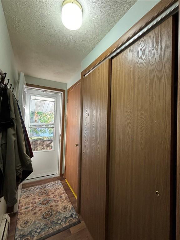 doorway to outside with a textured ceiling, wood finished floors, and a baseboard heating unit