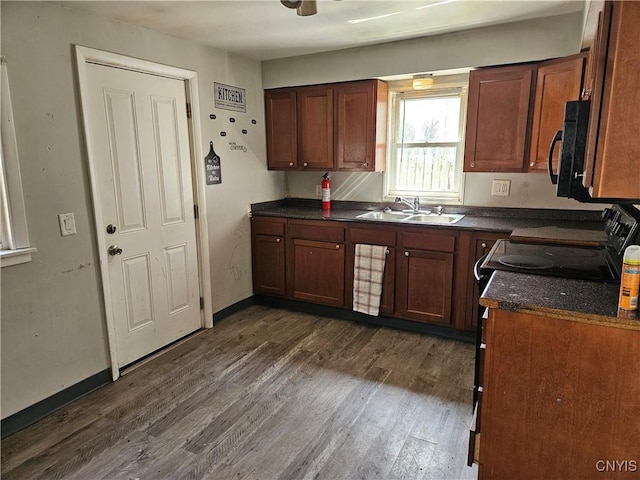 kitchen featuring dark countertops, a sink, black microwave, baseboards, and dark wood-style flooring