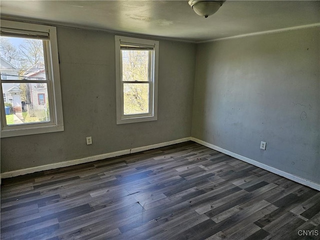 empty room featuring crown molding, baseboards, a wealth of natural light, and dark wood finished floors