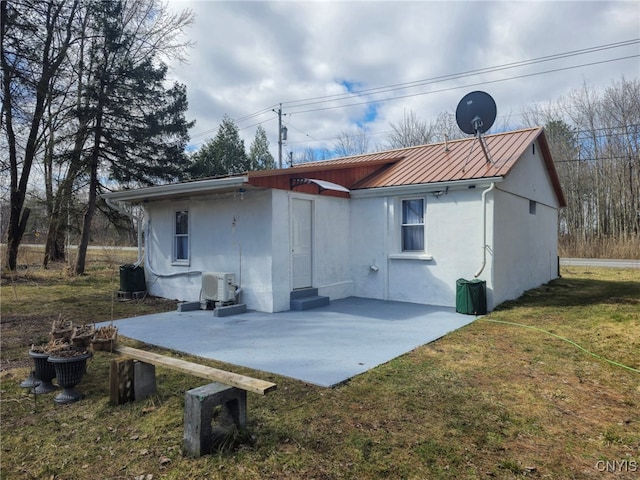rear view of property featuring a standing seam roof, stucco siding, metal roof, a patio, and a lawn