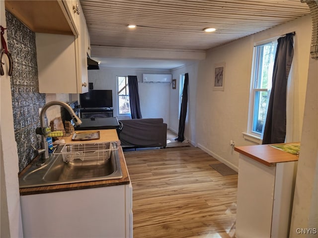 kitchen with white cabinets, light wood-style flooring, a sink, an AC wall unit, and wood ceiling