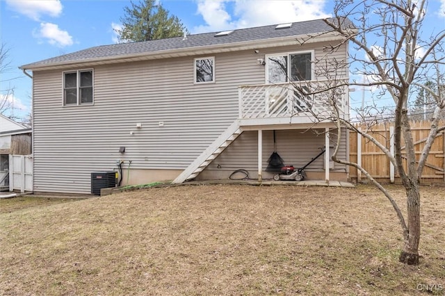 rear view of property with central air condition unit, fence, stairs, roof with shingles, and a lawn