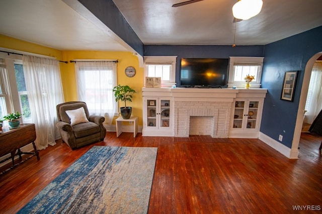 living area with arched walkways, a ceiling fan, wood finished floors, and baseboards