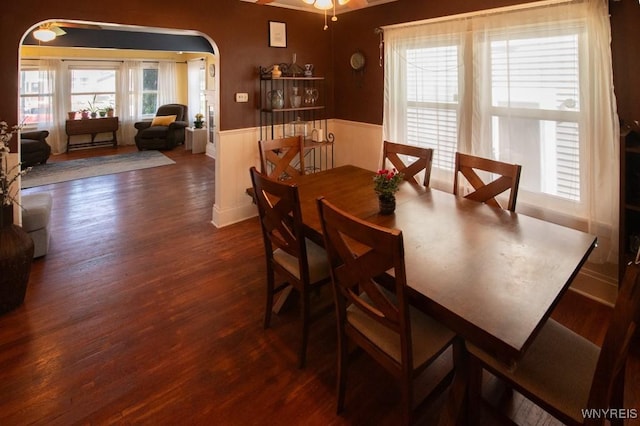 dining area featuring arched walkways, wood finished floors, a wainscoted wall, and a ceiling fan