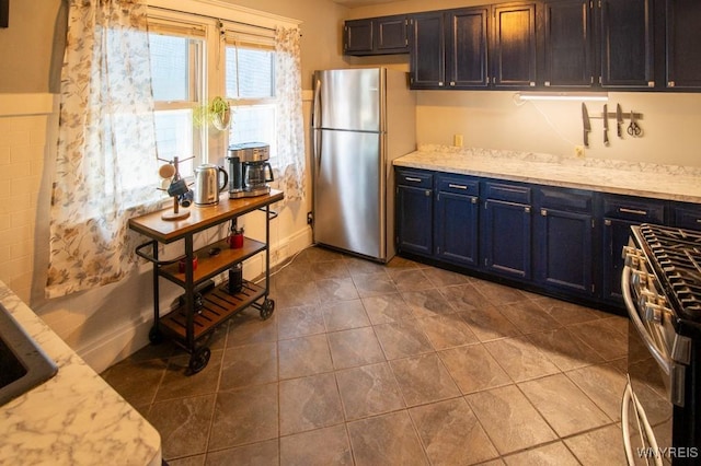 kitchen featuring blue cabinets, light stone countertops, stainless steel appliances, and dark tile patterned flooring