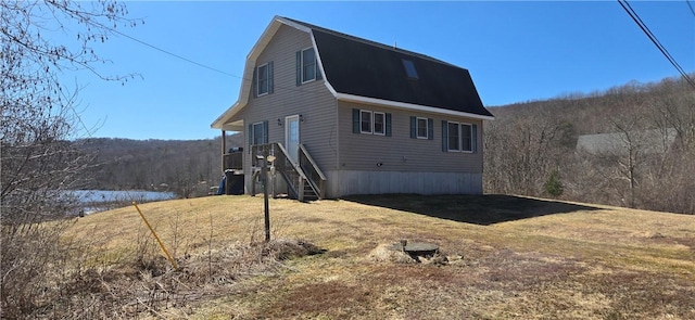 exterior space featuring a gambrel roof, a yard, and a view of trees
