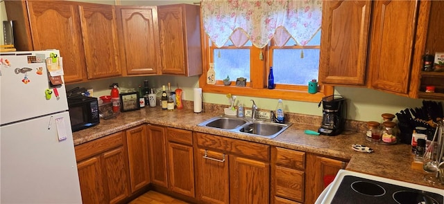 kitchen featuring electric stove, a sink, freestanding refrigerator, black microwave, and brown cabinets