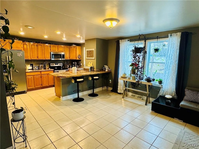 673 Cooper St, Watertown-City, NY 13601 - kitchen with light tile patterned flooring, a peninsula, brown cabinets, appliances with stainless steel finishes, and a kitchen breakfast bar