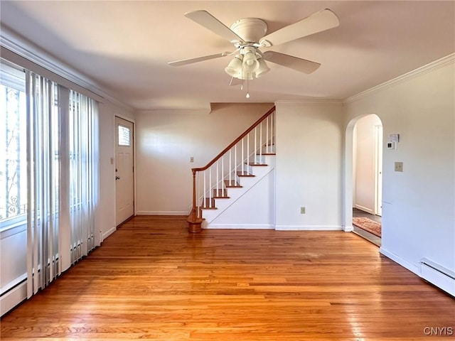 entrance foyer featuring light wood finished floors, crown molding, arched walkways, and a baseboard heating unit