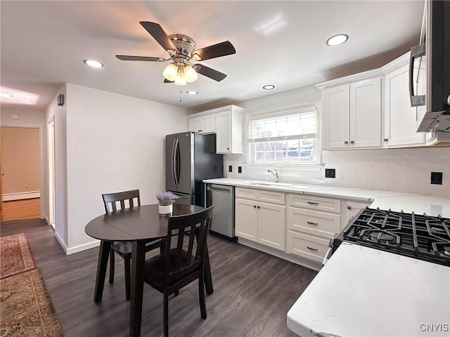 kitchen with stainless steel appliances, decorative backsplash, a sink, a baseboard radiator, and a ceiling fan