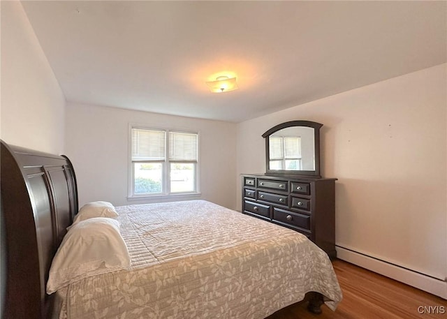 bedroom featuring wood finished floors, multiple windows, and a baseboard radiator