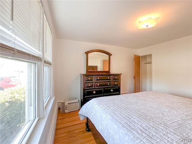 bedroom featuring a wall unit AC, multiple windows, and light wood-type flooring