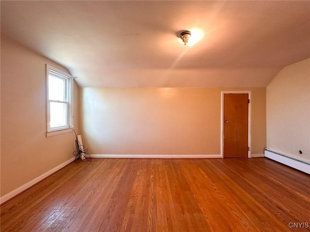 empty room featuring baseboards, wood finished floors, vaulted ceiling, and a baseboard heating unit