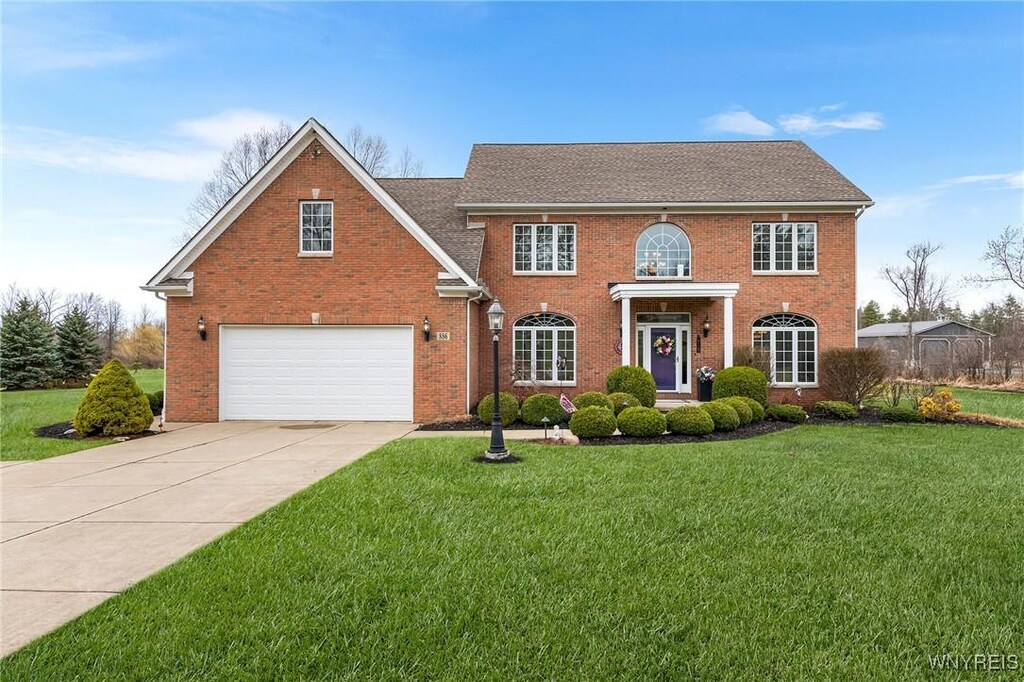 view of front of home featuring roof with shingles, driveway, a front yard, brick siding, and a garage