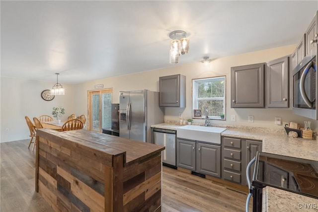 kitchen with decorative light fixtures, light wood-type flooring, gray cabinets, stainless steel appliances, and a sink