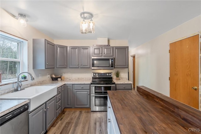 kitchen featuring a sink, wood finished floors, gray cabinetry, butcher block counters, and stainless steel appliances