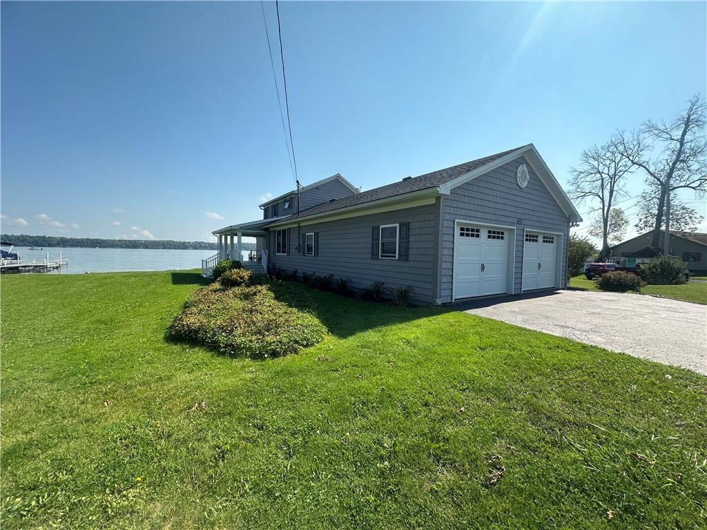 view of side of property featuring aphalt driveway, a water view, an attached garage, and a yard