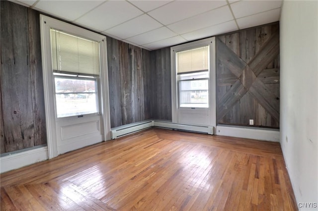 unfurnished room featuring a healthy amount of sunlight, a paneled ceiling, a baseboard heating unit, and hardwood / wood-style floors