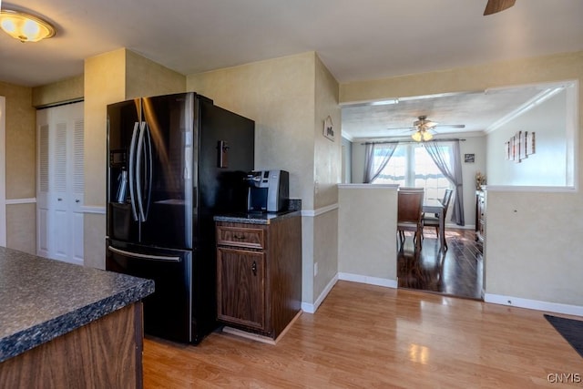 kitchen featuring black fridge with ice dispenser, light wood-style flooring, ceiling fan, ornamental molding, and dark countertops