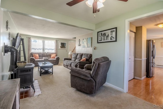 carpeted living room featuring baseboards, a wood stove, and a ceiling fan