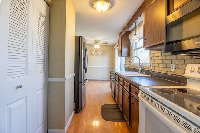kitchen featuring stainless steel appliances, a sink, dark countertops, a ceiling fan, and brown cabinetry