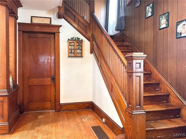 staircase featuring baseboards, visible vents, wooden walls, and wood finished floors