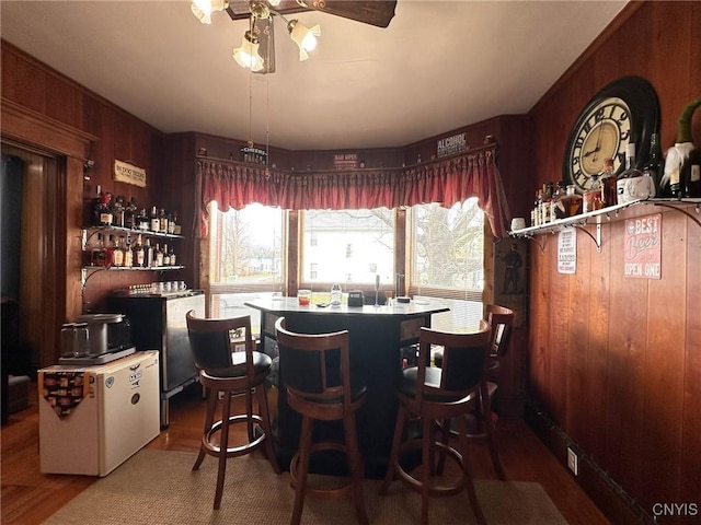 dining space with a bar, wooden walls, and ceiling fan