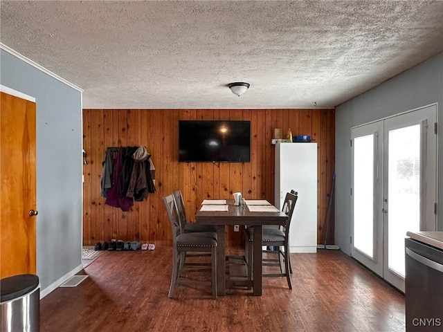 dining room with baseboards, a textured ceiling, wood finished floors, and wood walls