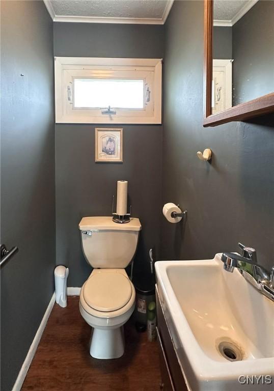 bathroom featuring crown molding, toilet, baseboards, a sink, and wood finished floors