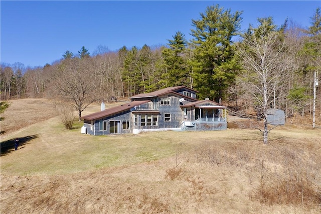 back of house featuring a chimney, a wooded view, and a yard