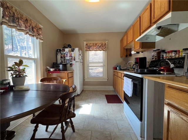 kitchen featuring freestanding refrigerator, range with electric stovetop, brown cabinetry, under cabinet range hood, and baseboards