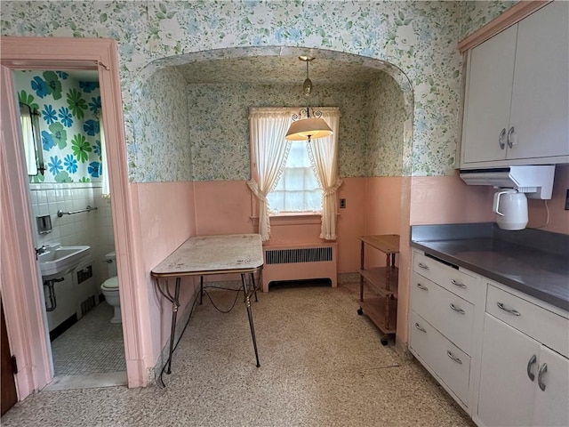 174 N Bennett St, Bradford-City, PA 16701 - kitchen with wallpapered walls, radiator heating unit, a wainscoted wall, dark countertops, and white cabinetry