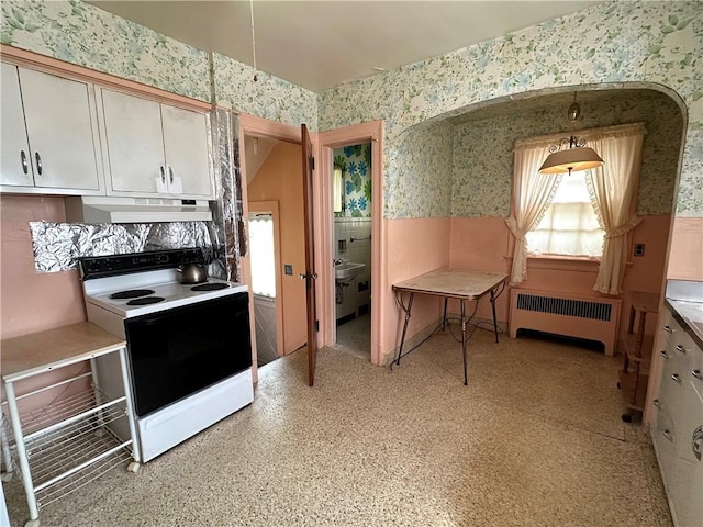 174 N Bennett St, Bradford-City, PA 16701 - kitchen with radiator, range with electric stovetop, wallpapered walls, under cabinet range hood, and white cabinetry