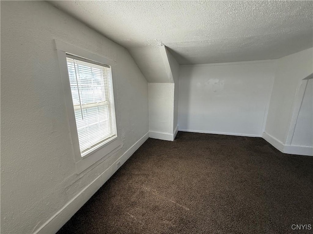 318 Academy St, Watertown-City, NY 13601 - bonus room with a textured ceiling, dark carpet, a textured wall, vaulted ceiling, and baseboards