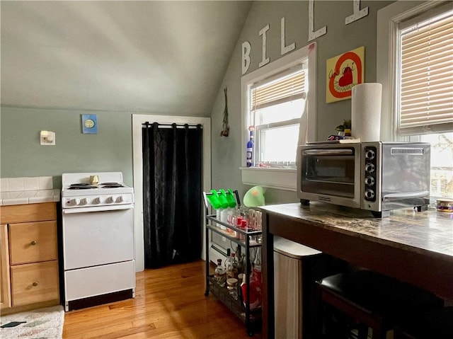 kitchen with lofted ceiling, a toaster, electric stove, tile countertops, and light wood-style floors