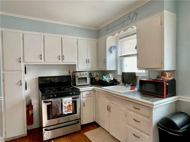 kitchen with tile counters, a sink, stainless steel gas range, white cabinets, and wood finished floors