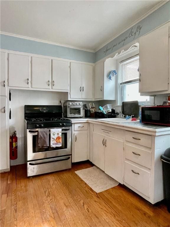 kitchen featuring crown molding, stainless steel range with gas stovetop, white cabinetry, black microwave, and light wood-style floors