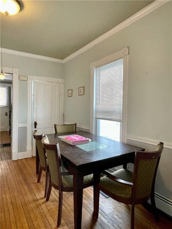 dining space with baseboard heating, crown molding, and light wood-style floors