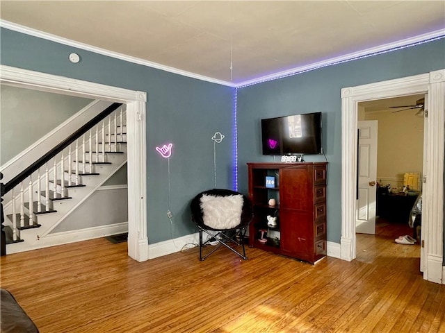sitting room featuring baseboards, stairs, ornamental molding, and wood finished floors