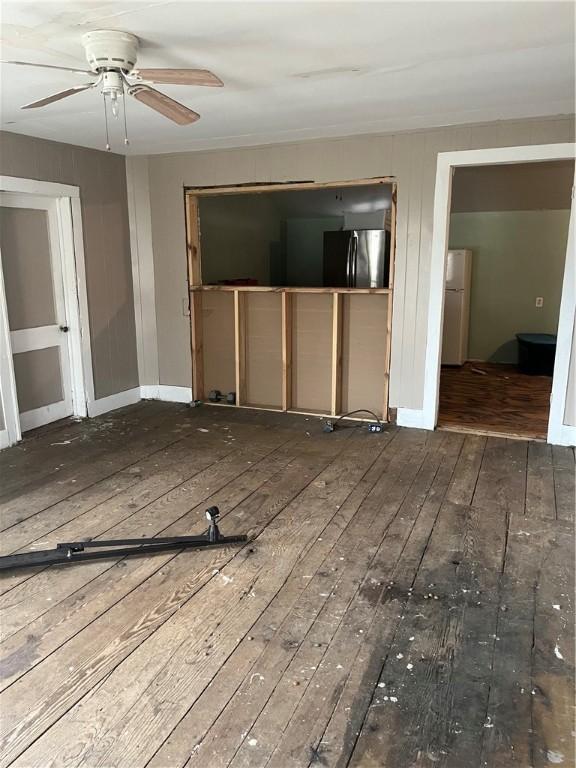 unfurnished living room featuring wood-type flooring, a ceiling fan, and baseboards