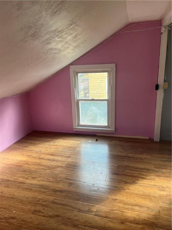 additional living space with a textured ceiling, lofted ceiling, and wood finished floors