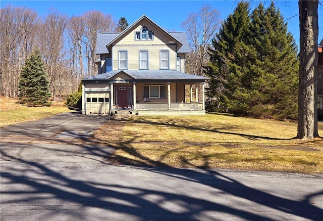 victorian-style house featuring driveway, a front yard, covered porch, and an attached garage