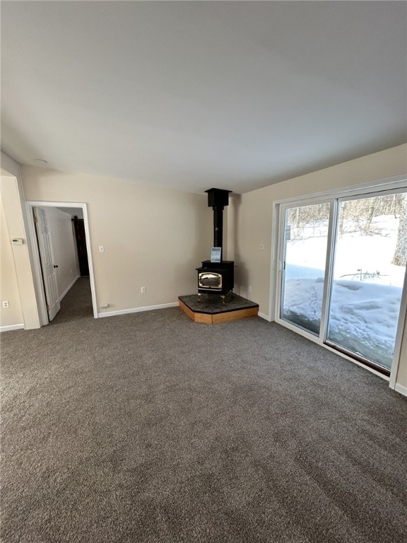 unfurnished living room with baseboards, dark colored carpet, and a wood stove