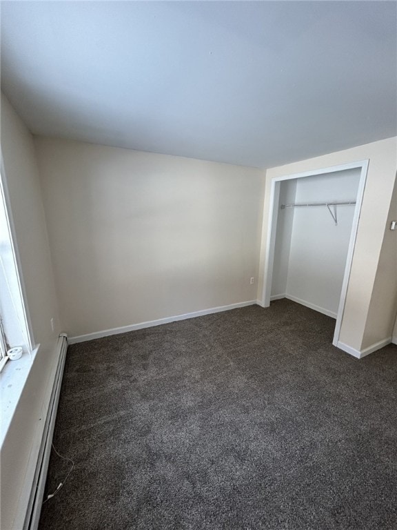 unfurnished bedroom featuring baseboards, dark carpet, a baseboard heating unit, and a closet