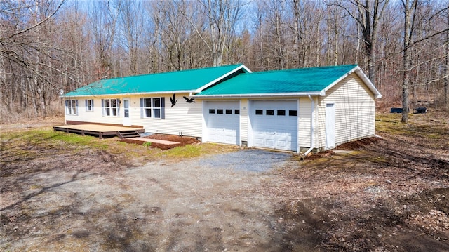 view of front of house with dirt driveway, metal roof, and an attached garage
